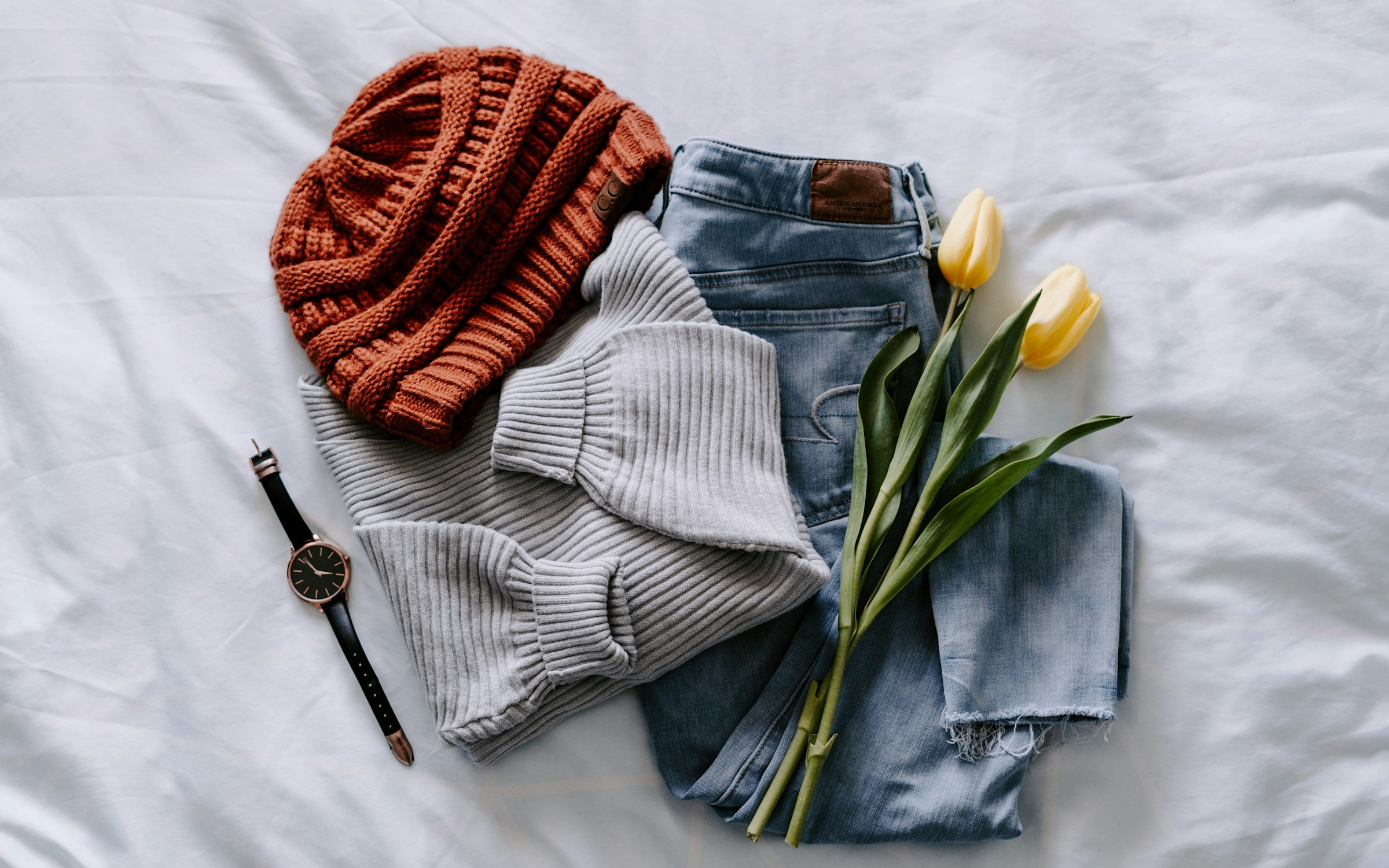 A minimal rail of neutral garments against a cream wall, softly lit.