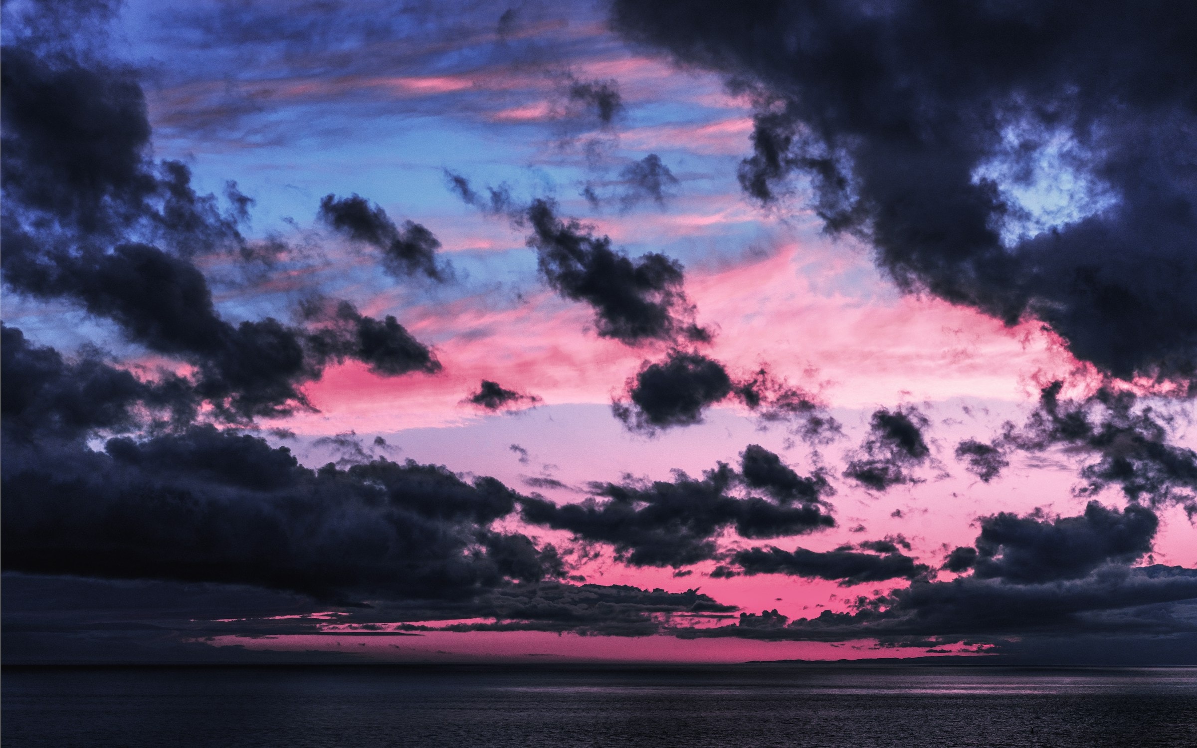 An open wardrobe partially emptied, with three piles of folded clothes on the floor in front of it.